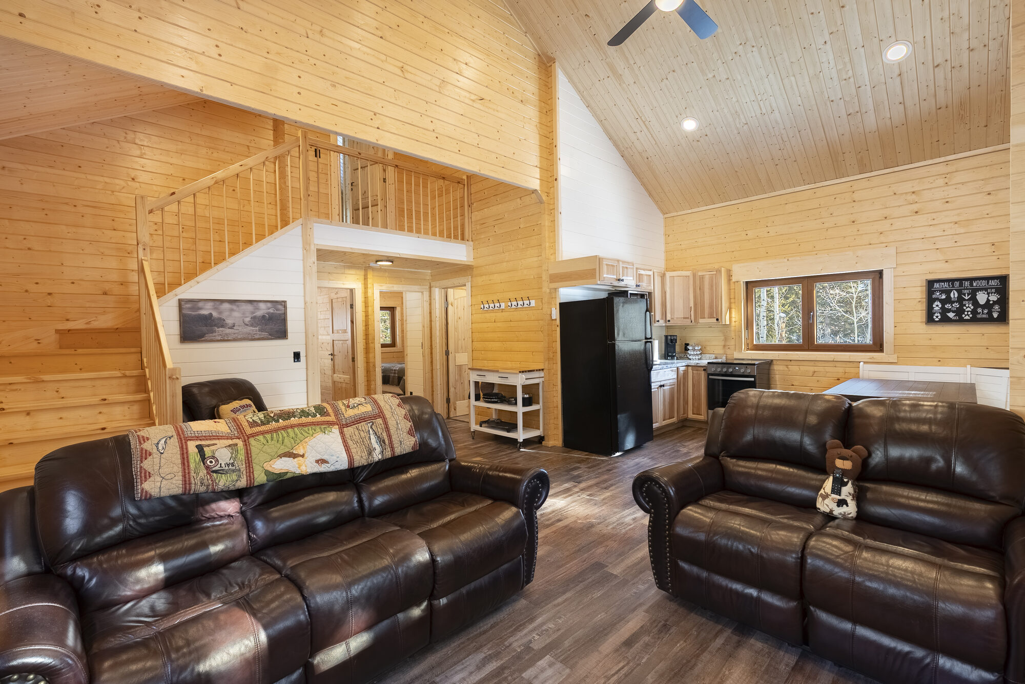 Log cabin great room with vaulted wood ceiling, loft, and leather sofas